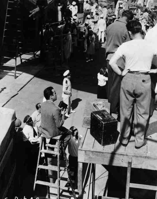 This interesting photo captures Bogart sitting on a tall ladder making some home movies of his experience on set. 